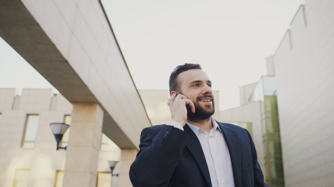 Smiling businessman in suit on phone call against modern architecture.